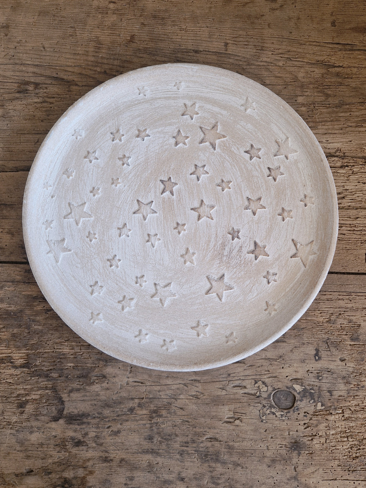 A round, off-white ceramic plate with an embossed star pattern, photographed from directly above on a rustic wooden surface.