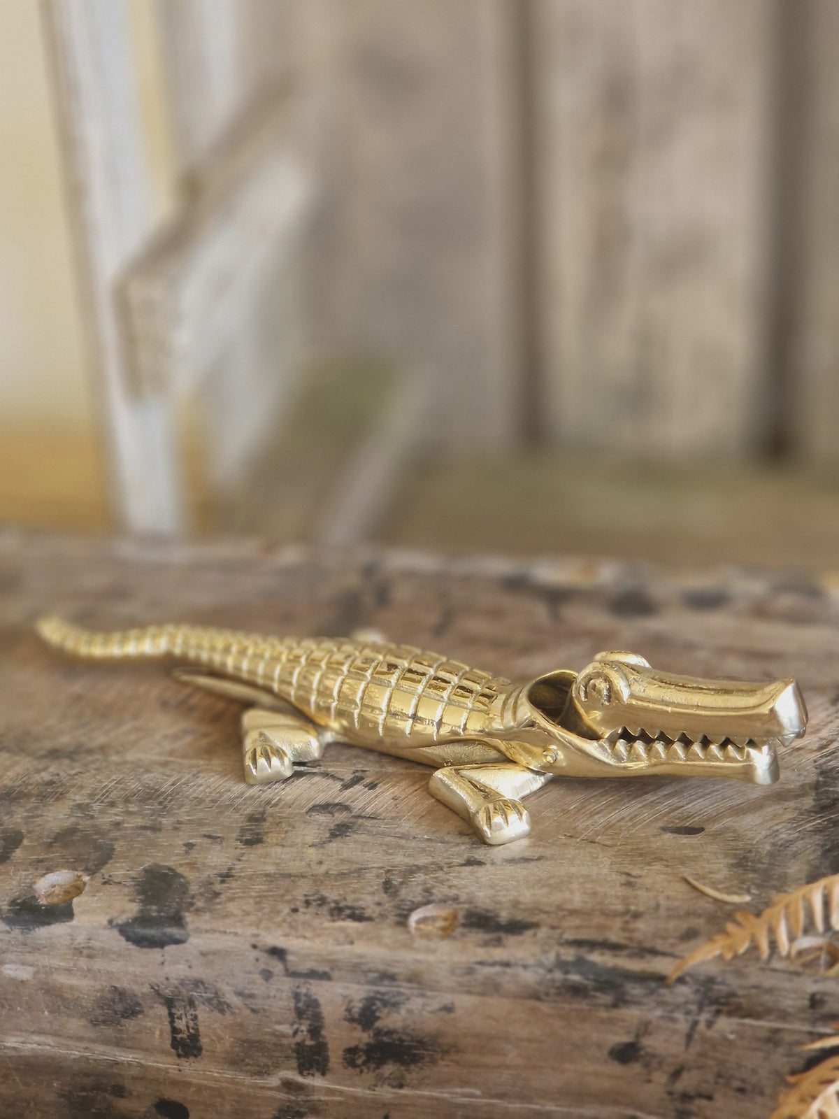 A small metallic alligator figurine in a polished gold finish, resting on a rustic weathered wooden surface with a blurred wooden background.