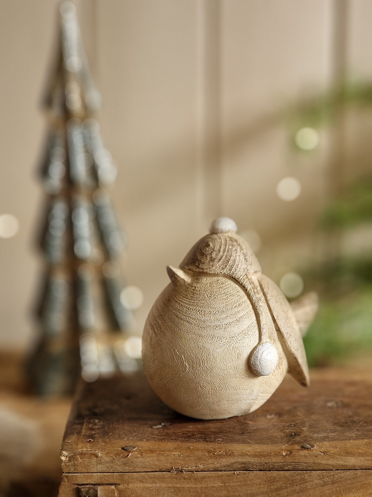A close-up of a decorative ceramic owl figurine with white bead eyes, mounted on a rustic wooden post against a softly blurred beige background.