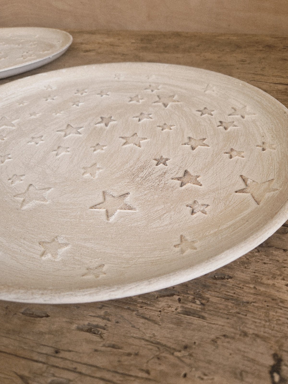 A round off-white ceramic plate with a textured, hand-painted finish and embossed star patterns, resting on a rustic wooden surface.