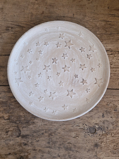 A round, off-white ceramic plate with an embossed star pattern, photographed from directly above on a rustic wooden surface.